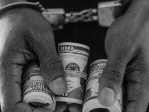 person in handcuff holding rolled dollar bills